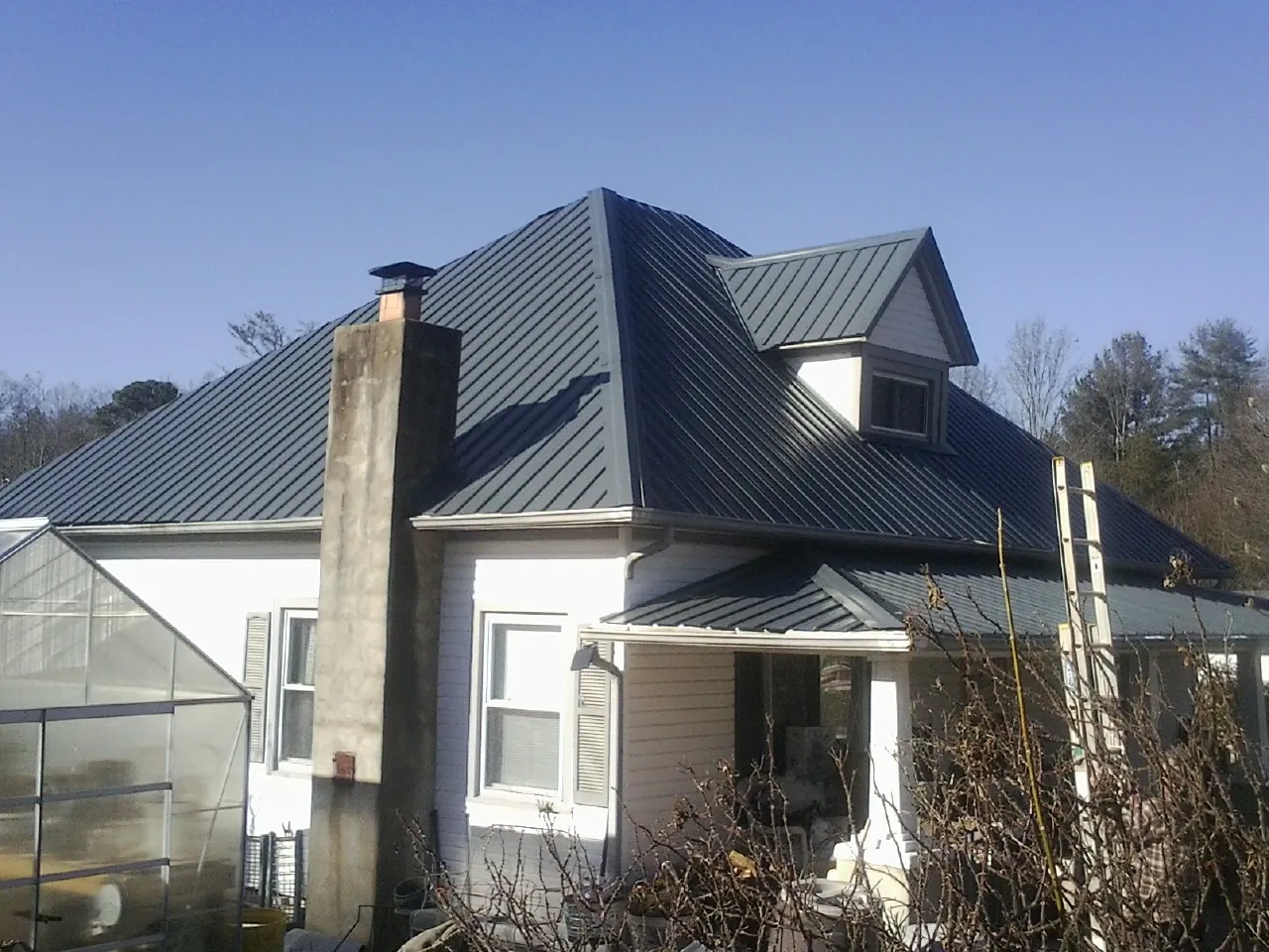 Dark blue standing seam metal roof on a white farmhouse with dormer — Slate & Tile Roof Repair by Roofing Brothers in Stanford
