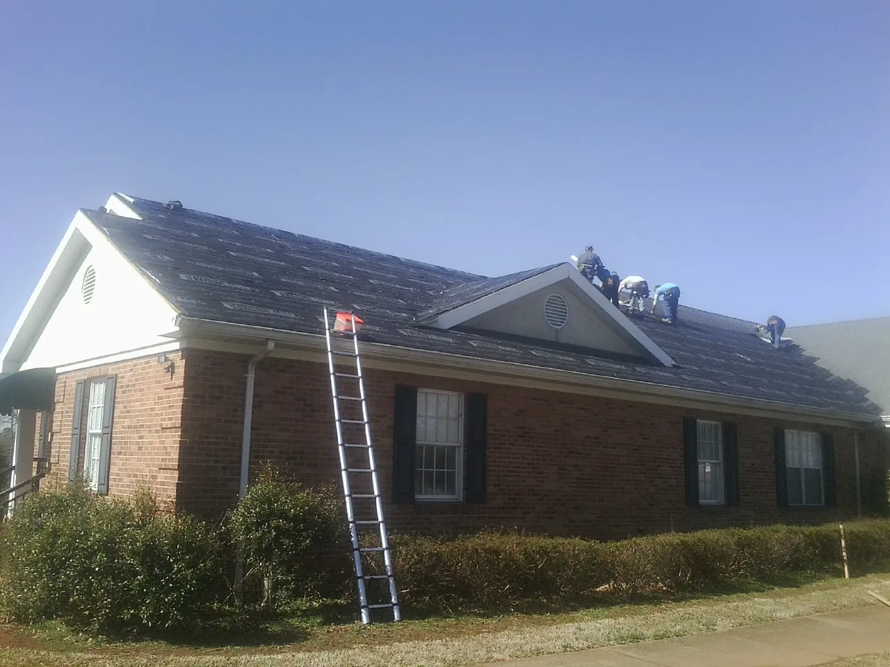 Crew tearing shingles off a brick ranch roof with a ladder set — Metal Roof Repair work by our crew in Stanford