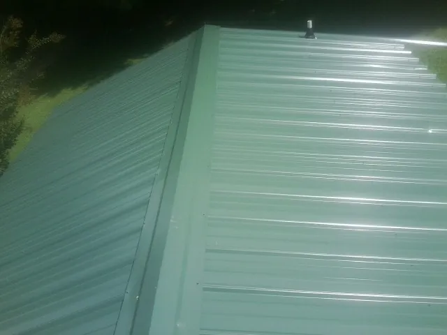 New green metal panels meeting at the ridge of a roof — Flat Roof Repair work by our crew in Stanford