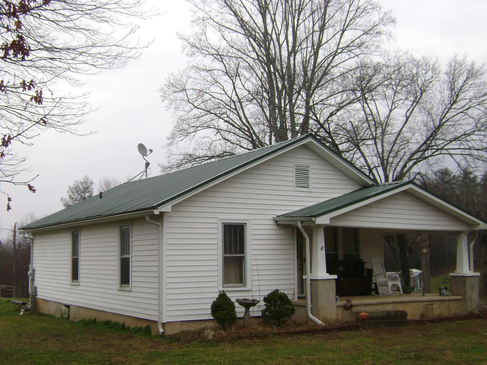 Green metal roof on a white bungalow with a side porch in Stanford